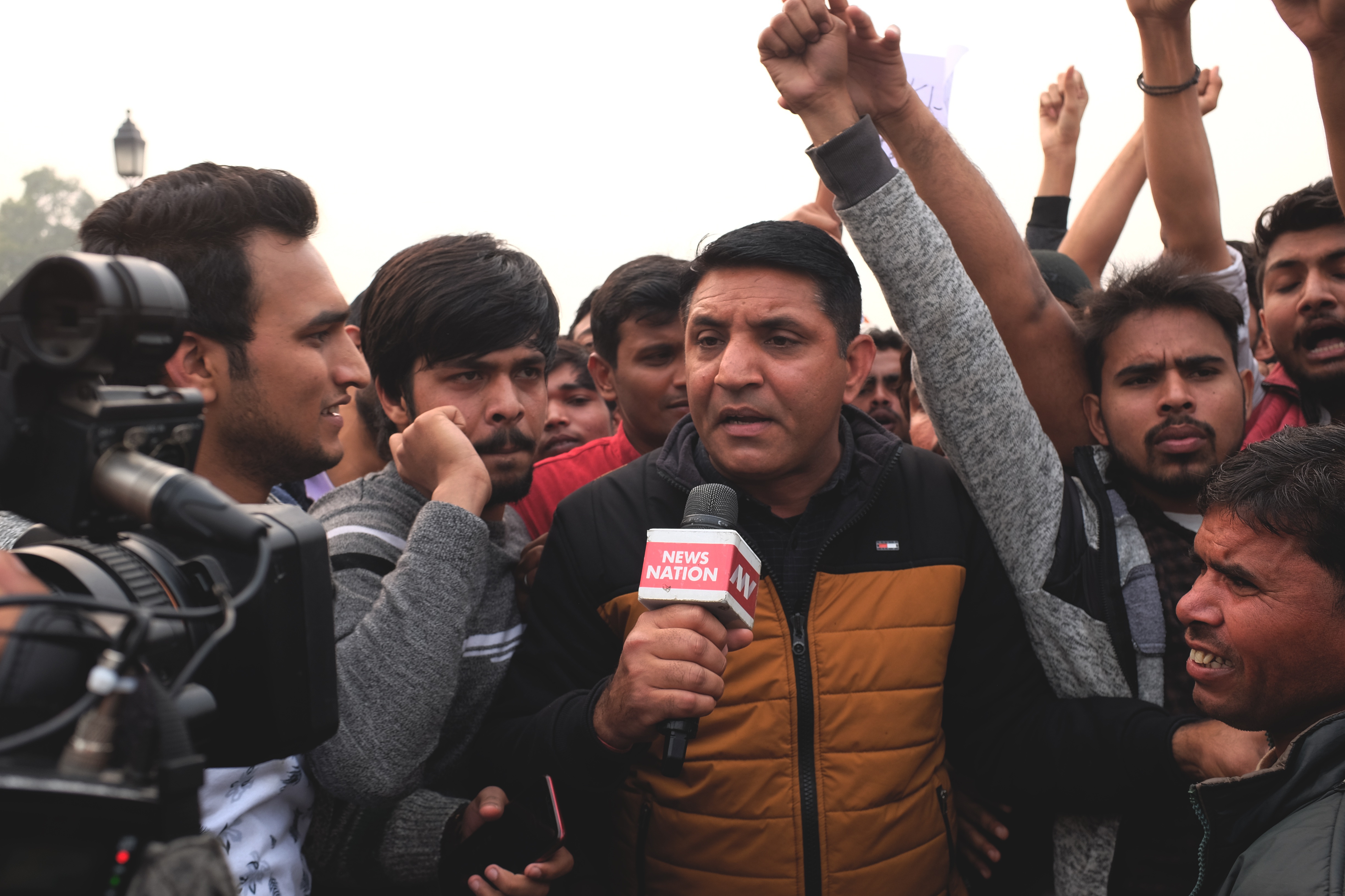 A journalist holding a microphone, reporting live in the middle of a crowd