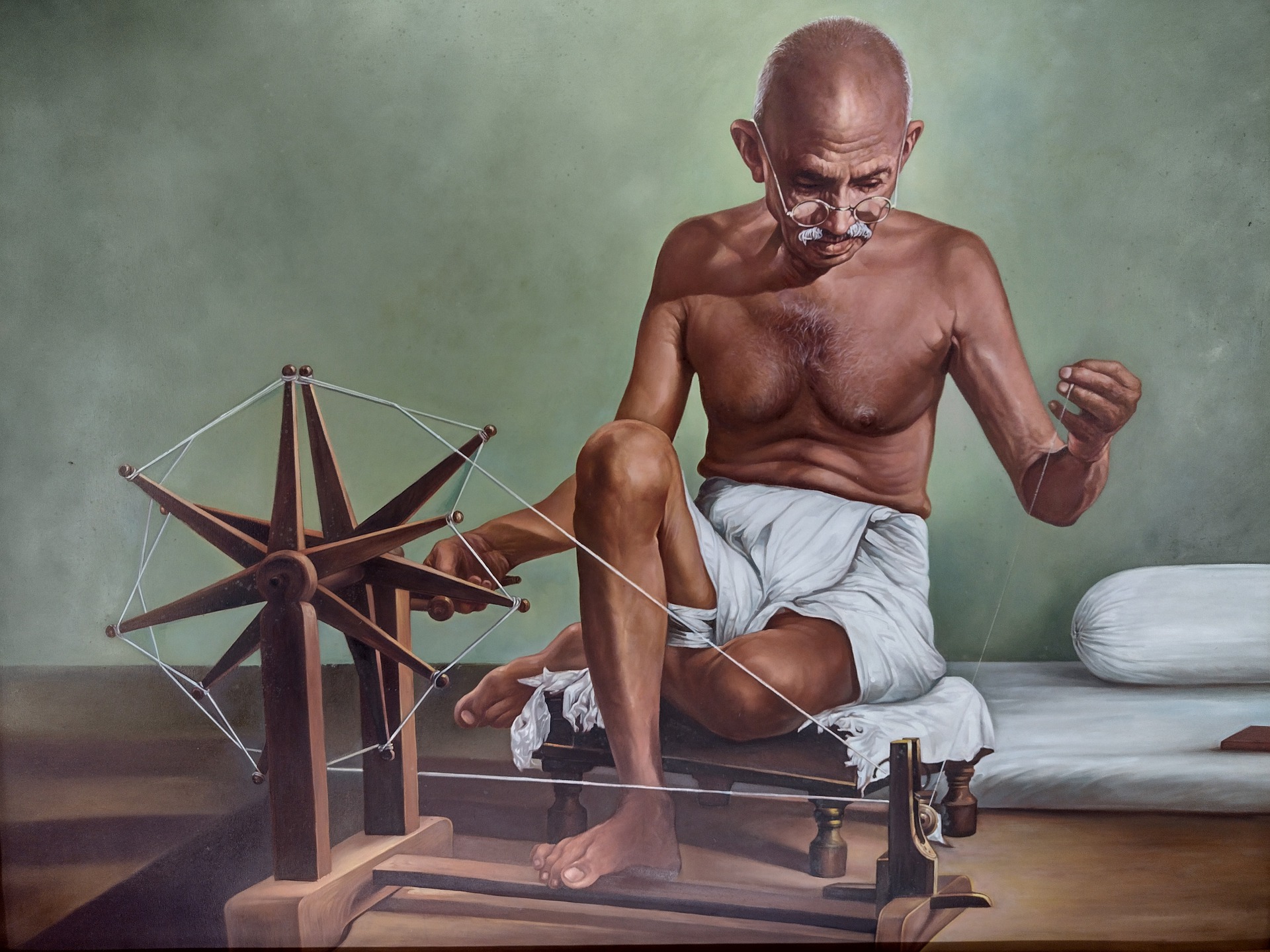 A painting of Gandhi sitting and spinning thread on a charkha (spinning wheel)