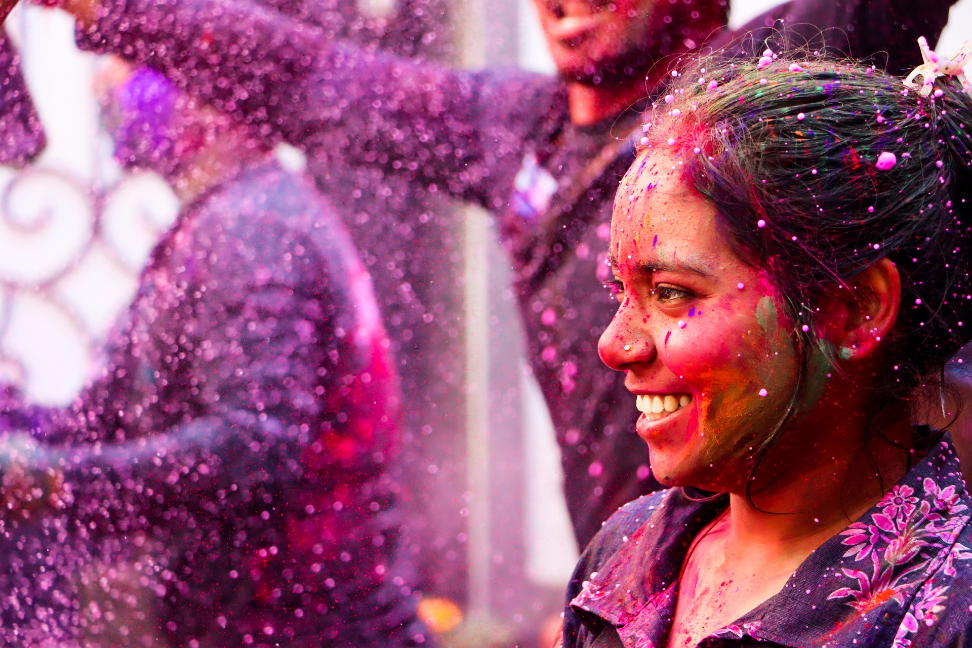 A young woman covered in colourful powder, smiling, during the Holi festival