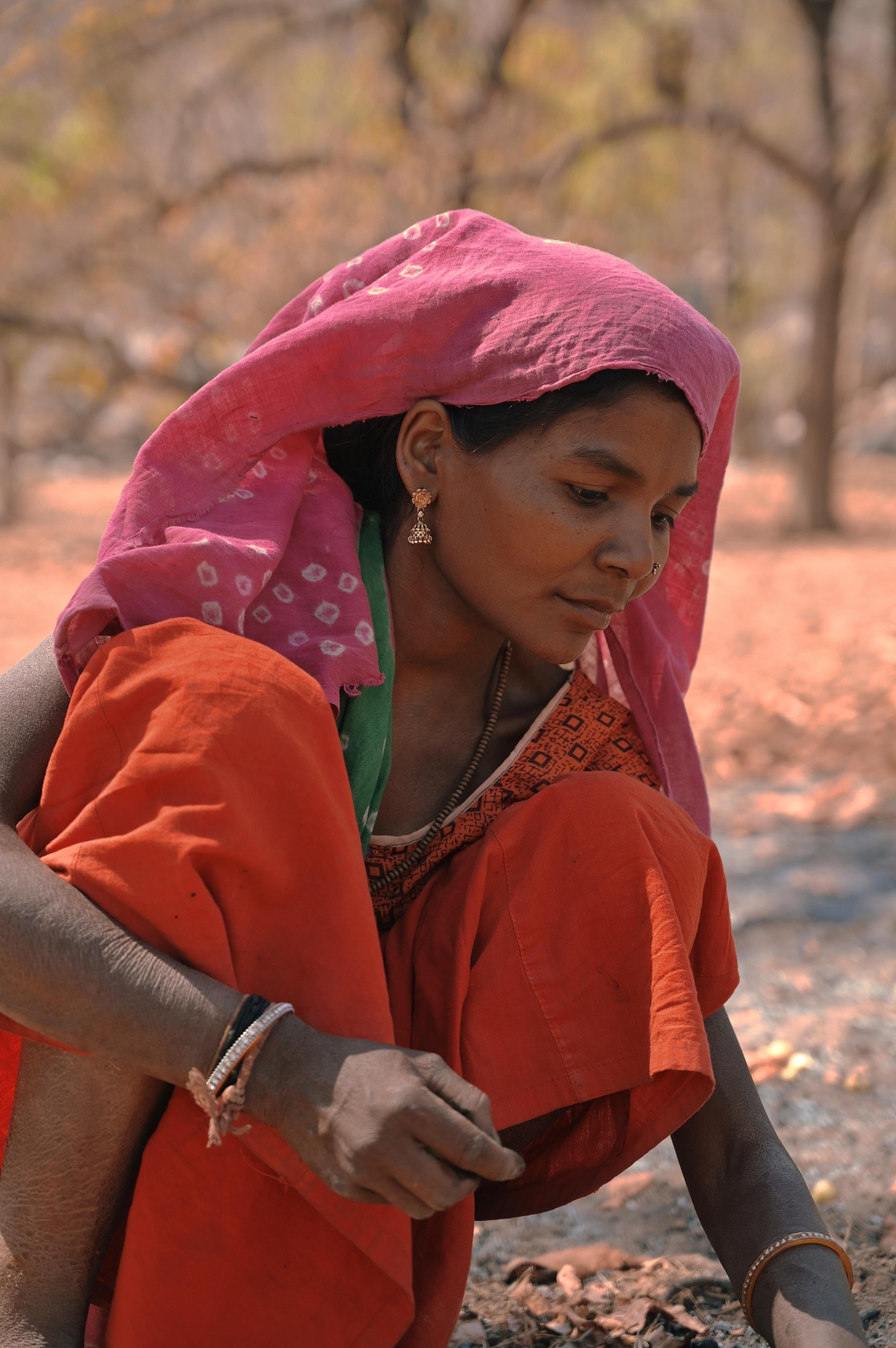 A woman in a pink headscarf and orange sari working outdoors in a rural setting