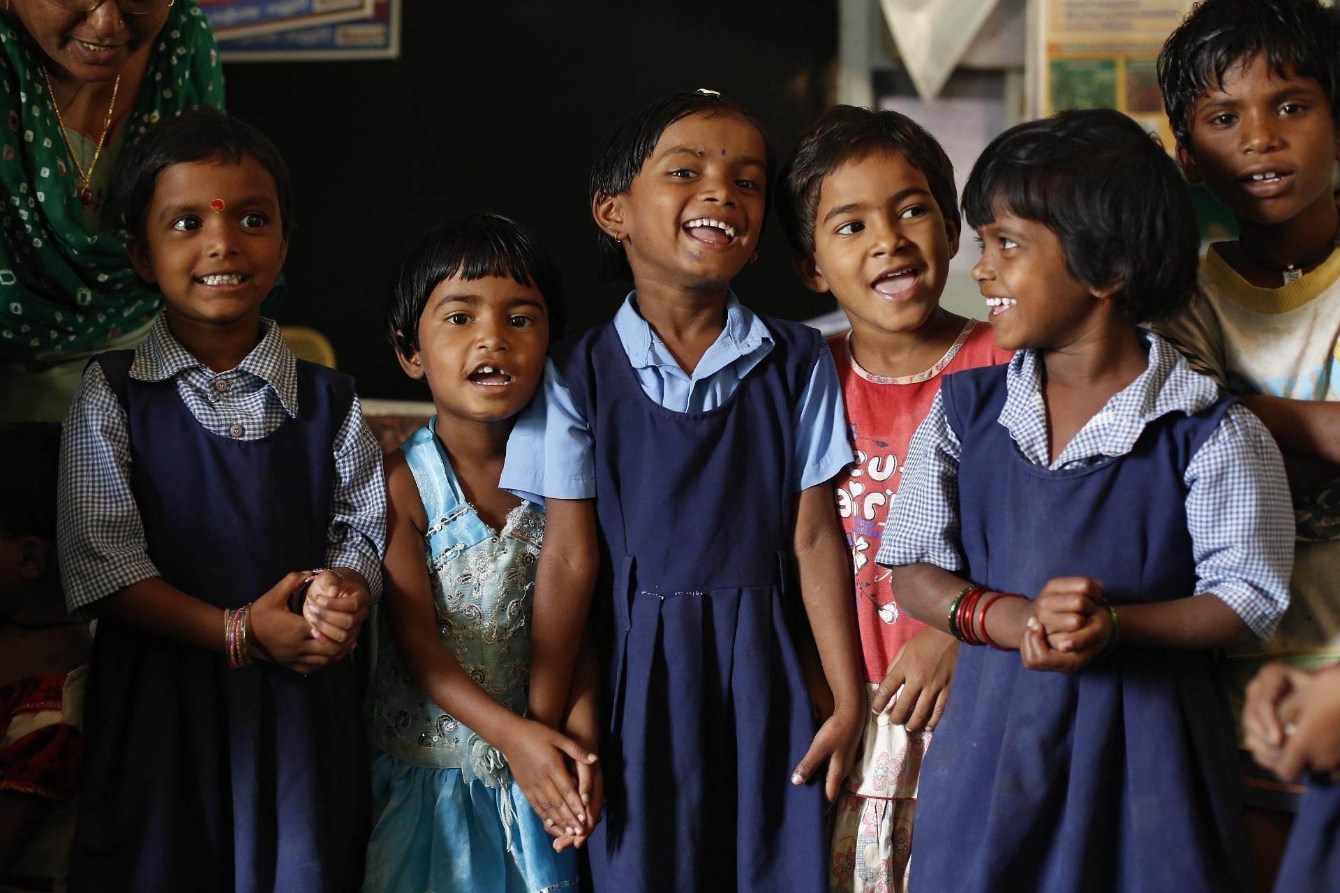 Schoolchildren in blue uniforms laughing together in a classroom