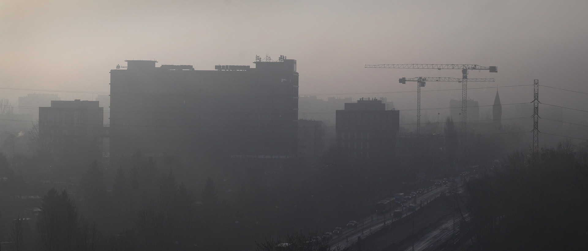A city skyline with buildings and construction cranes fading into thick haze