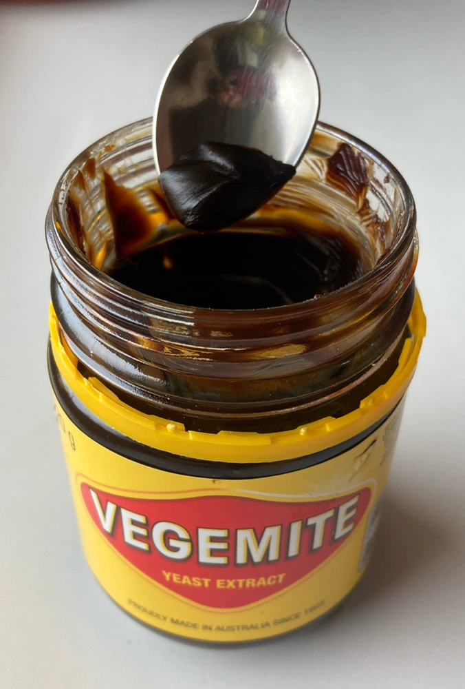 A jar of Vegemite with a spoon scooping out the thick, dark brown paste.